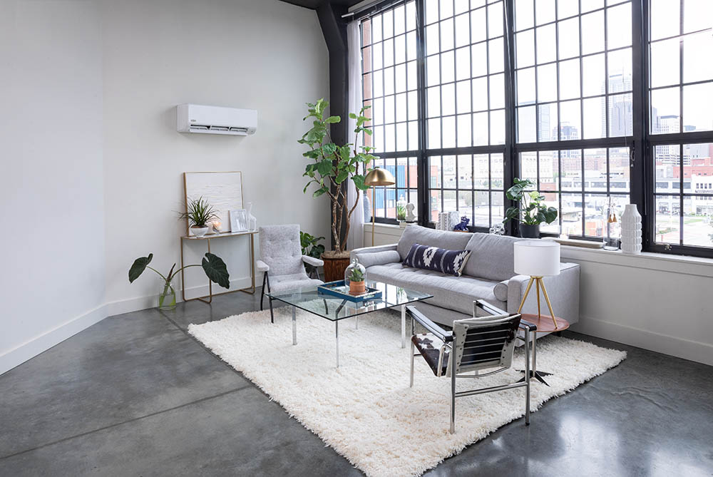 A living room with a large window, a white sectional sofa, and a gray rug.